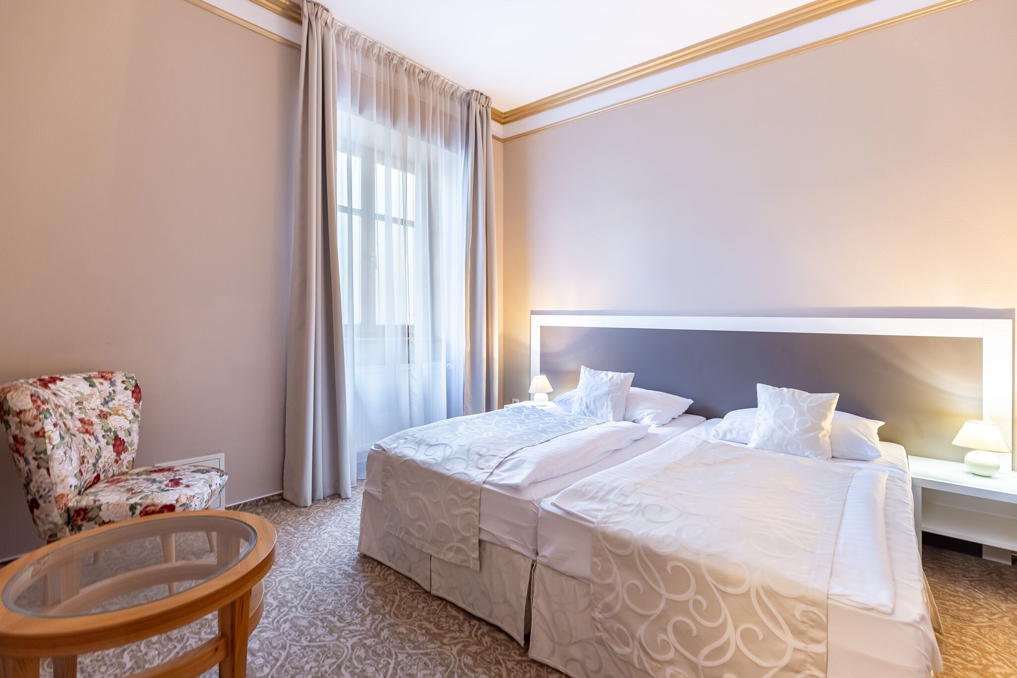 A hotel room with a large bed, a chair, a small table, and a window with curtains.