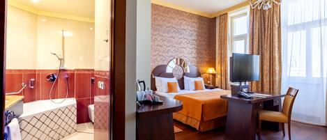 A hotel room with a shower, toilet, bed, desk, and TV.