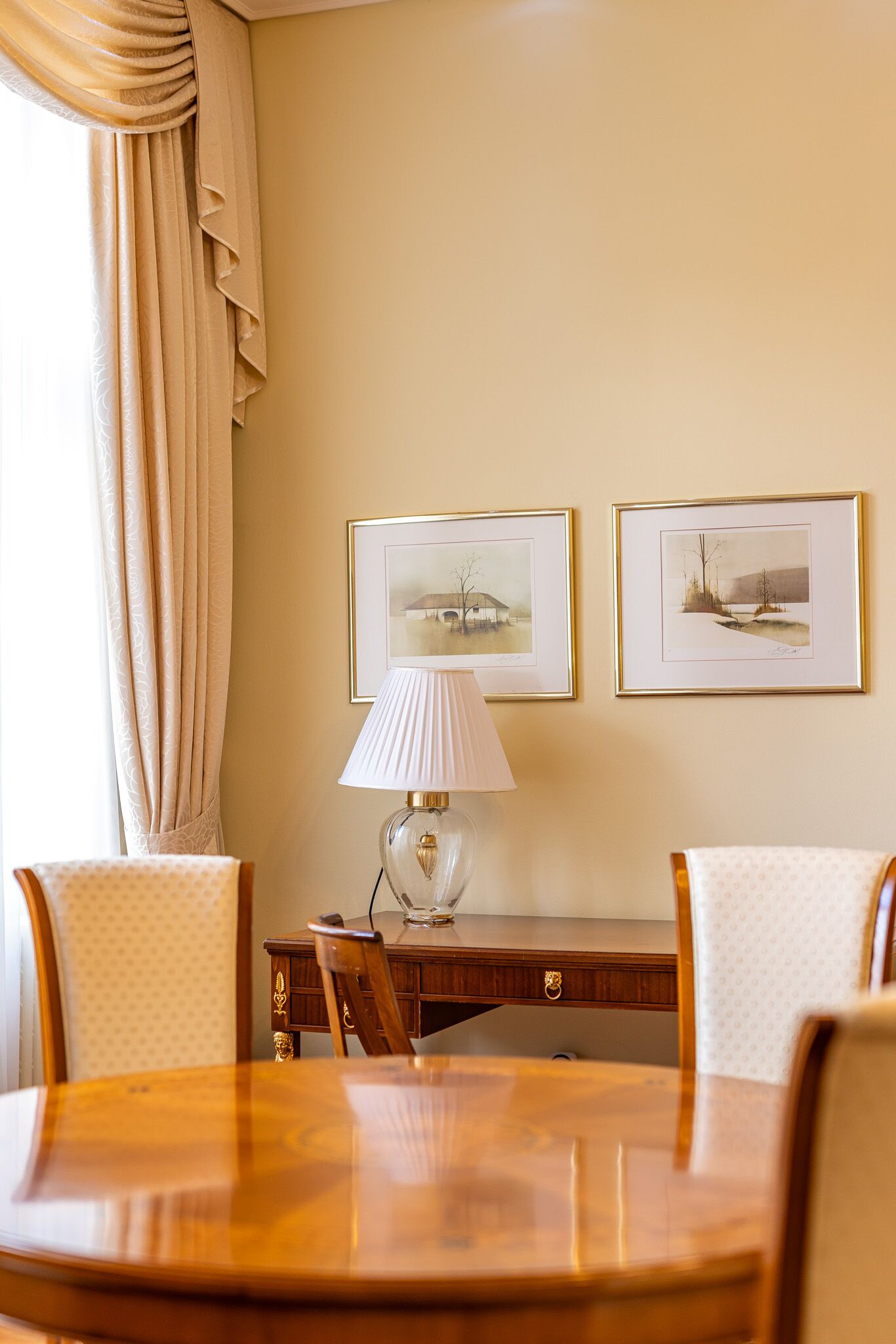 Un comedor con una mesa de madera, dos sillas, una lámpara y dos cuadros en la pared.