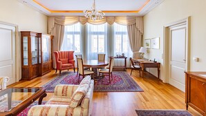 Amplia sala de estar con un sofá grande, una mesa de comedor con sillas, un sillón rojo, un aparador de madera y una araña.