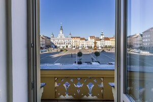 Vista desde una ventana de un edificio con balcón, con vista a una plaza con edificios históricos y una fuente.