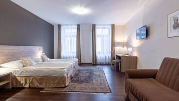 A hotel room with two beds, a desk, a chair, a TV, and a couch.