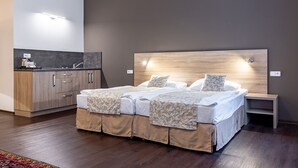Un dormitorio moderno con una cama grande, cabecera de madera, mesita de noche y una kitchenette integrada.