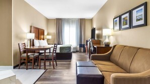 A hotel room with a dining area, a sofa, a TV, and a bed.
