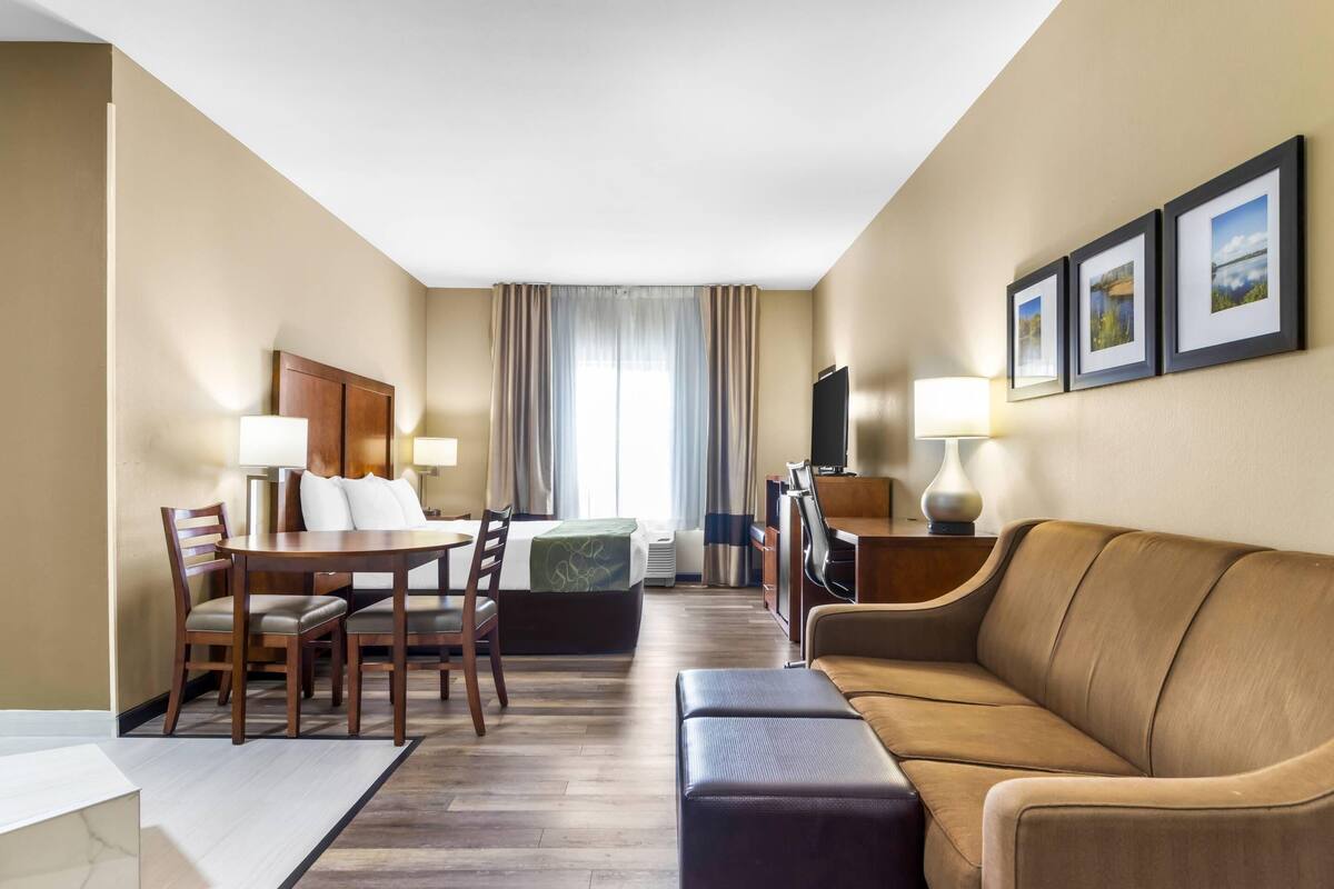 A hotel room with a dining area, a sofa, a TV, and a bed.