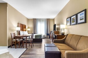 Habitación de hotel con zona de comedor, sofá, televisión y cama.