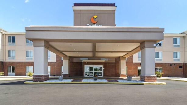 A hotel entrance with a covered walkway, brick facade, and a sign indicating the name 'Comfort'.