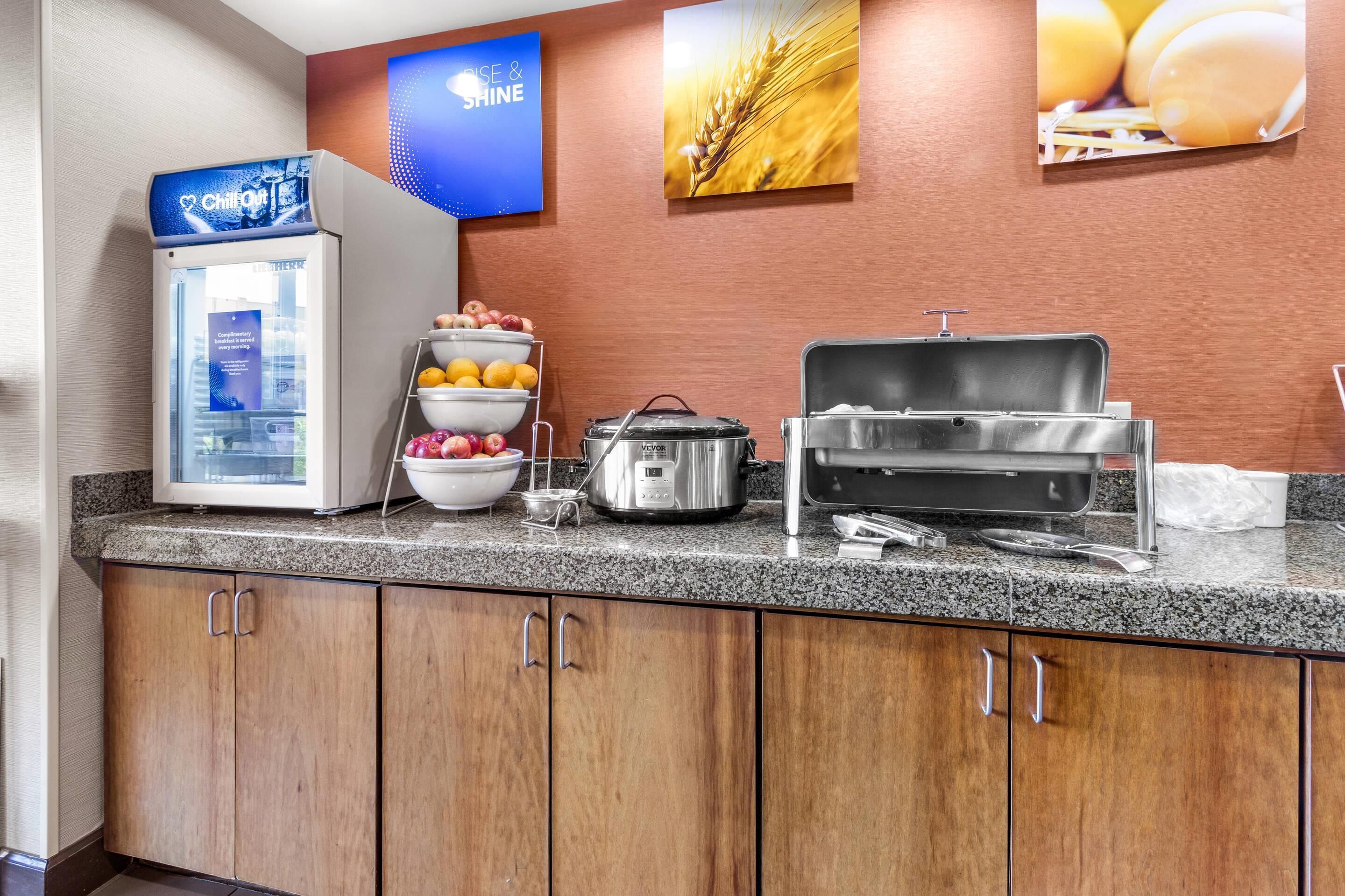 A breakfast bar with a refrigerator, bowls of fruit, a pot, and a coffee maker.