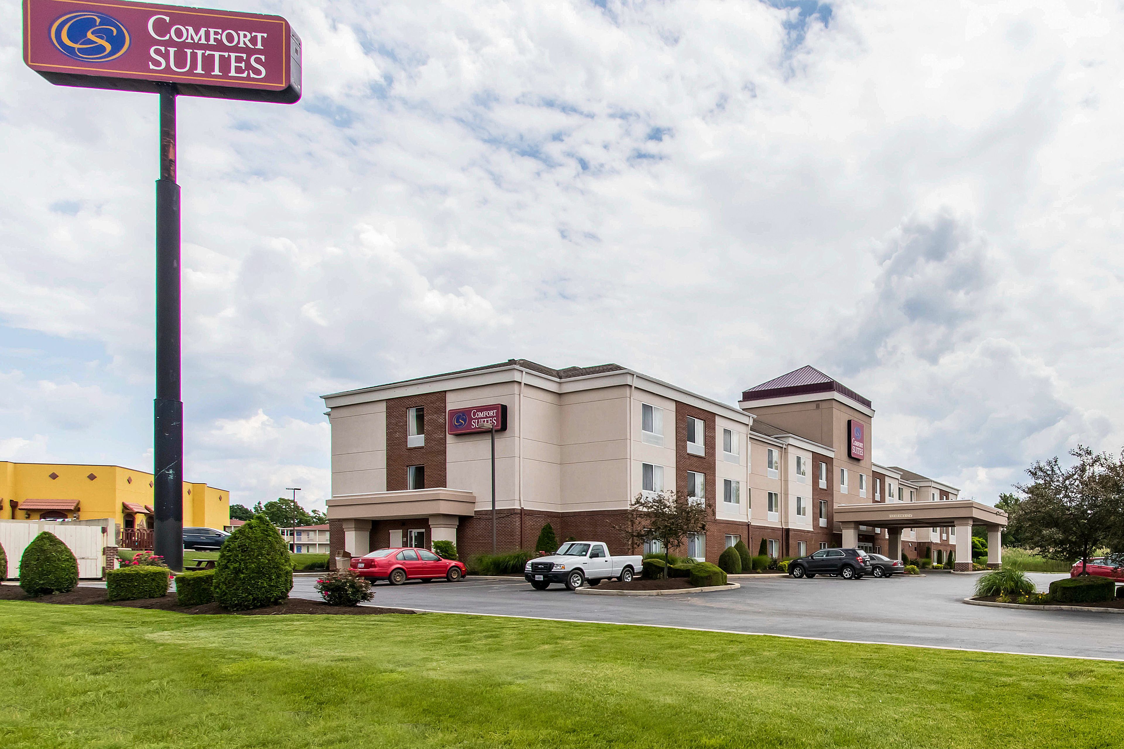 Un hotel Comfort Suites con fachada de ladrillo, varias ventanas y un estacionamiento con varios automóviles.
