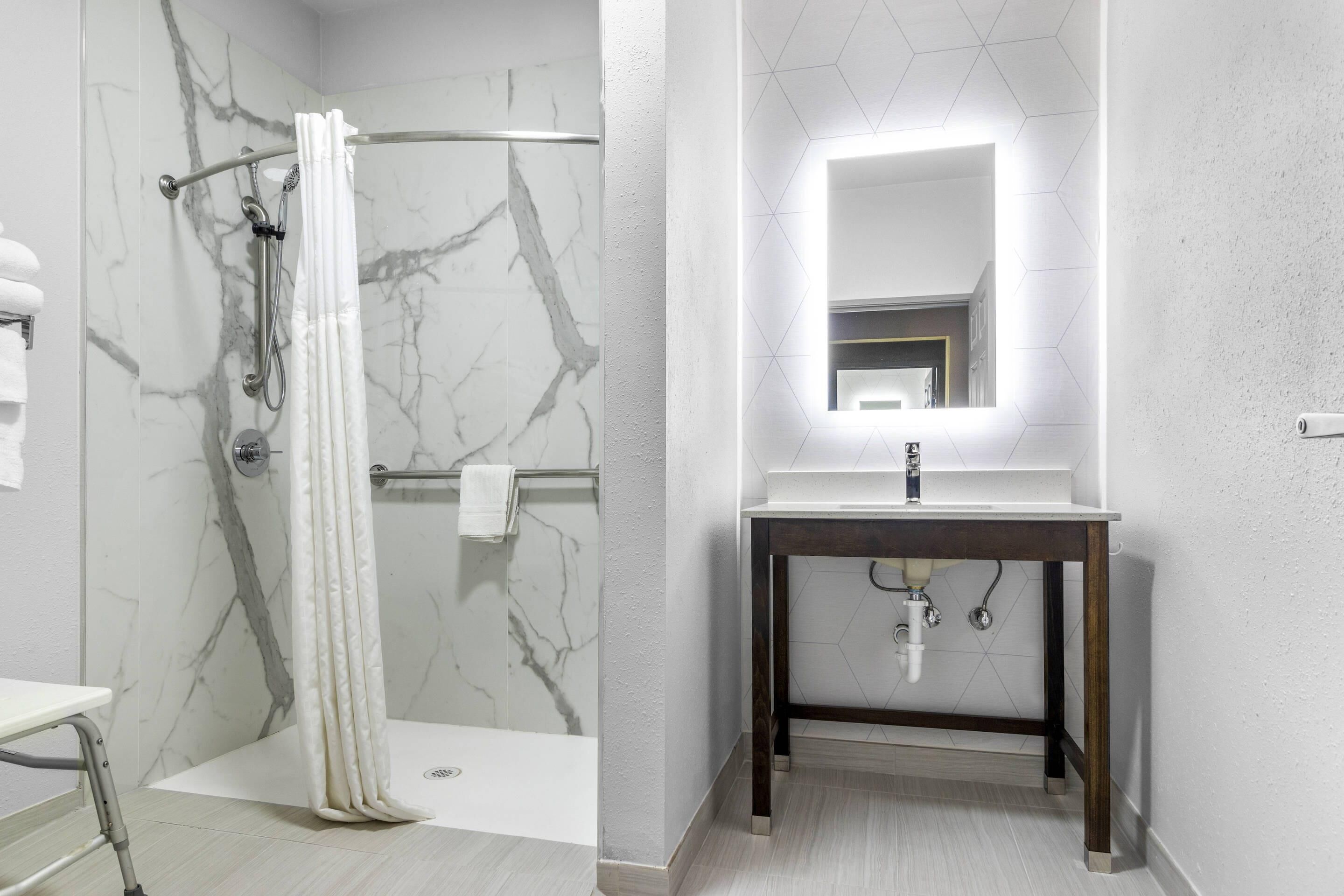 A modern bathroom with a marble shower, a vanity with a mirror, and a light fixture above the mirror.