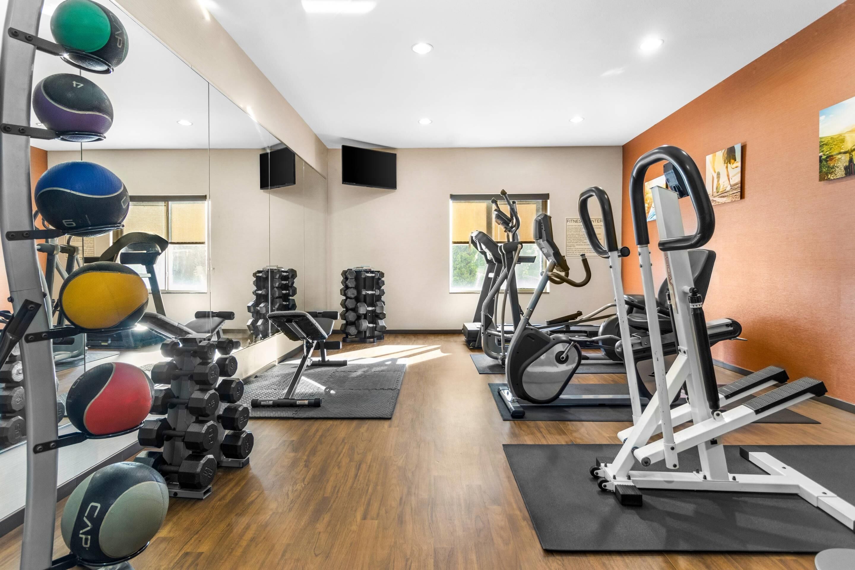 Un gimnasio con equipo de ejercicio, espejos y suelo de madera.