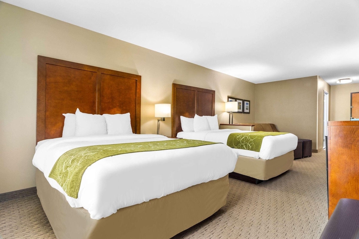 A hotel room with two beds, a desk, and a mirror.