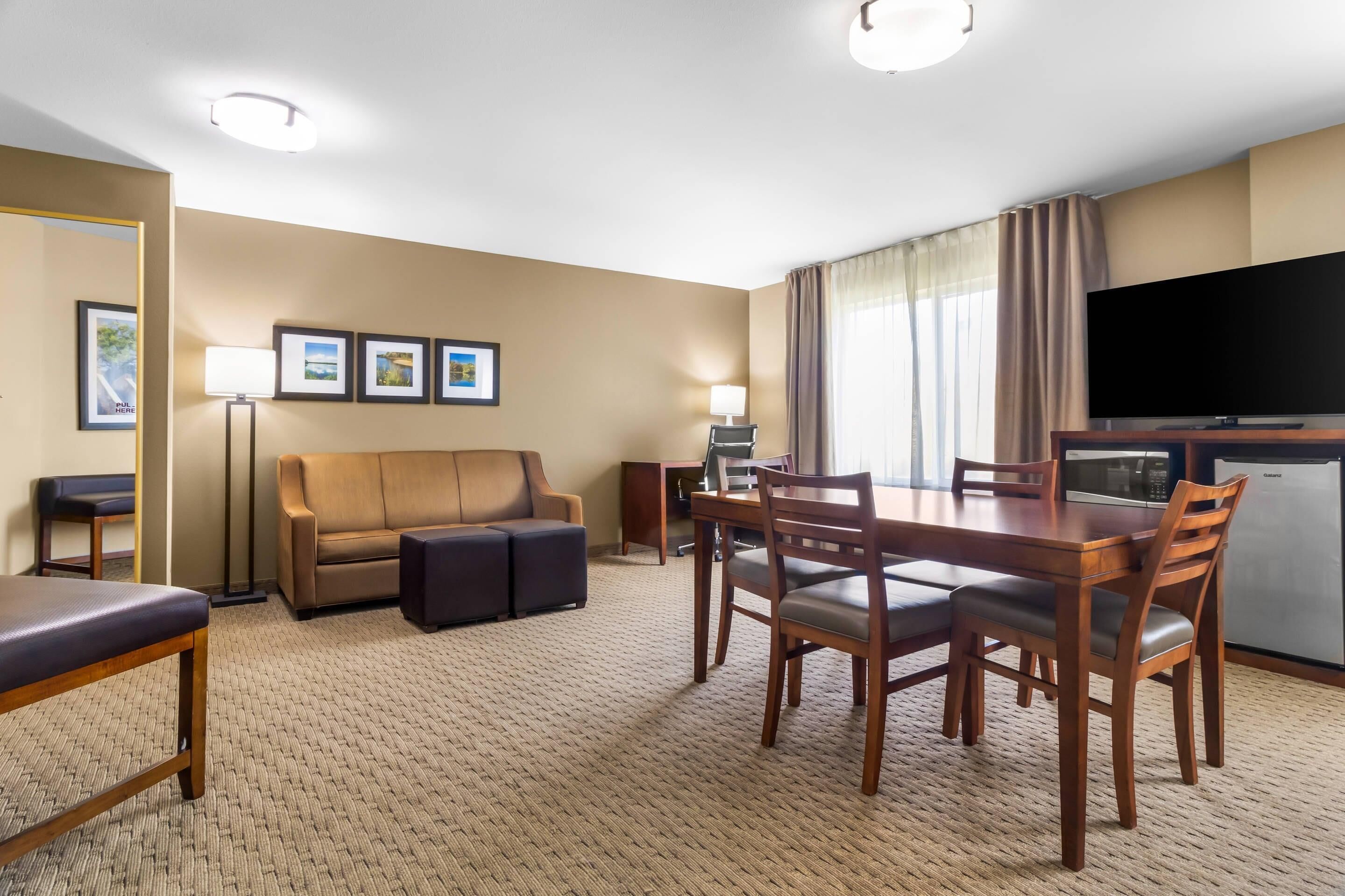 Ein Hotelzimmer mit Essbereich, einer Couch, einem Fernseher und einer Küchenzeile.
