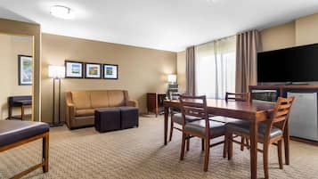 Ein Hotelzimmer mit Essbereich, einer Couch, einem Fernseher und einer Küchenzeile.