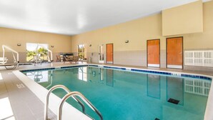 A swimming pool with a clear blue water, surrounded by a beige wall and doors.