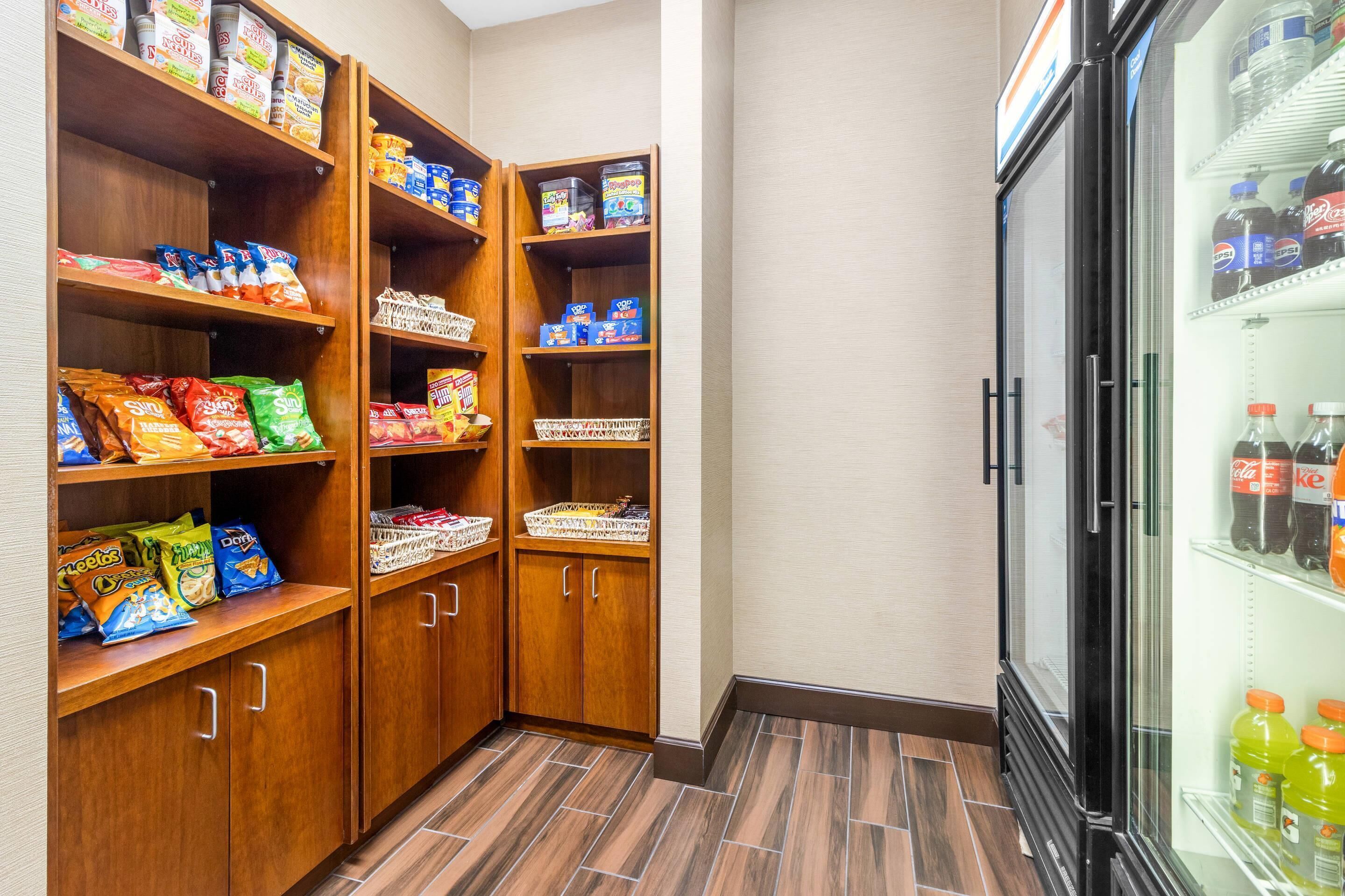 A well-organized pantry with shelves stocked with snacks and beverages, a refrigerator with drinks, and a tiled floor.