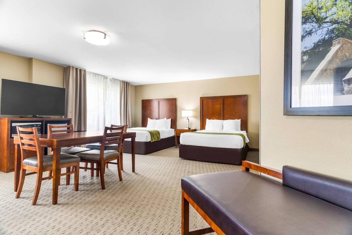 A hotel room with a dining area, a TV, two beds, and a large window.