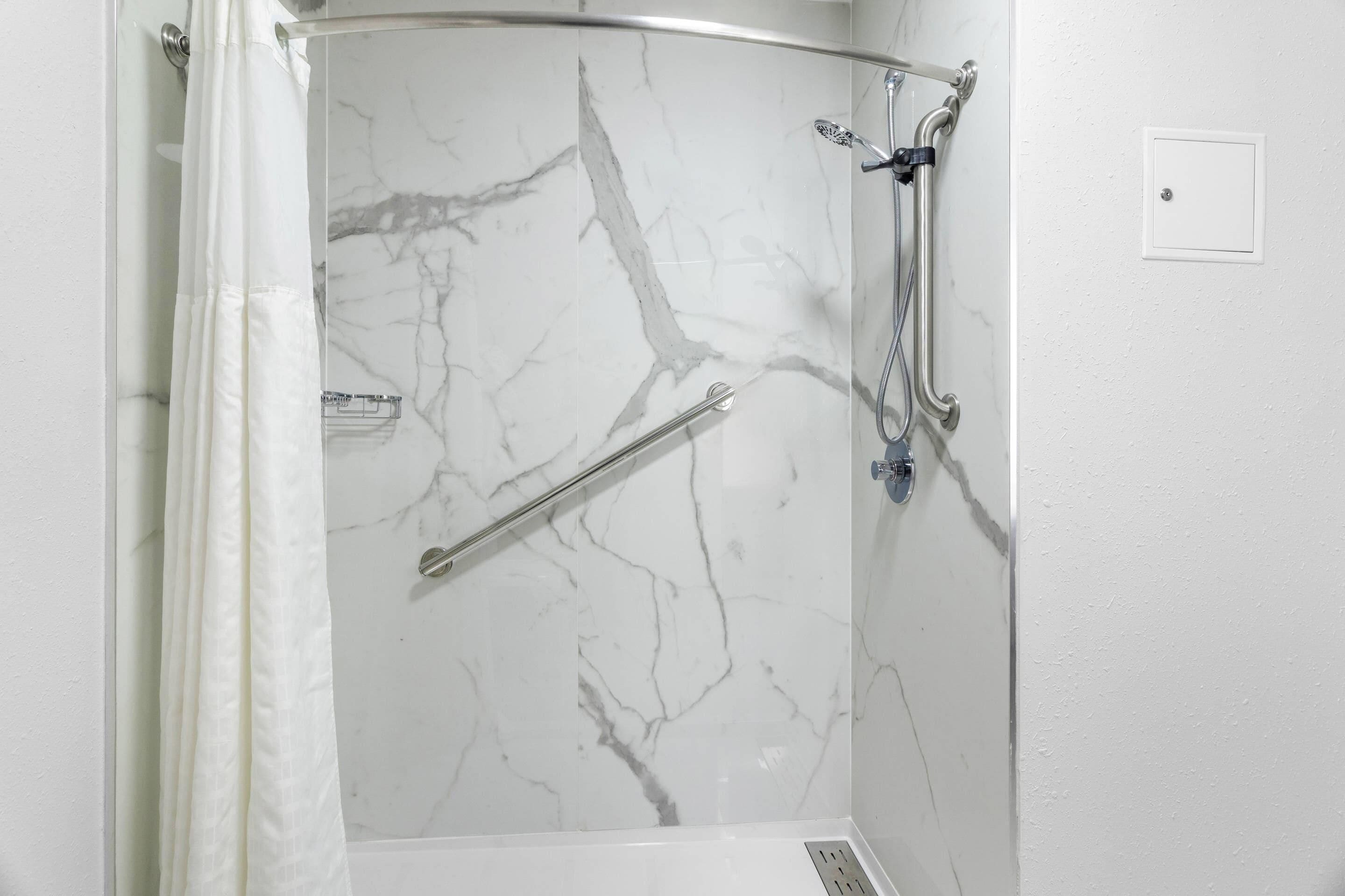 A shower with a marble wall, a handrail, and a showerhead.