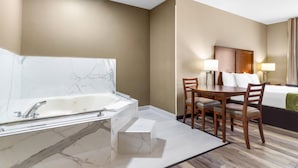 A hotel room with a marble bathtub, a wooden dining table with chairs, a bed with a headboard, and a nightstand with lamps. - Comfort Suites Mount Vernon (Mount Vernon)