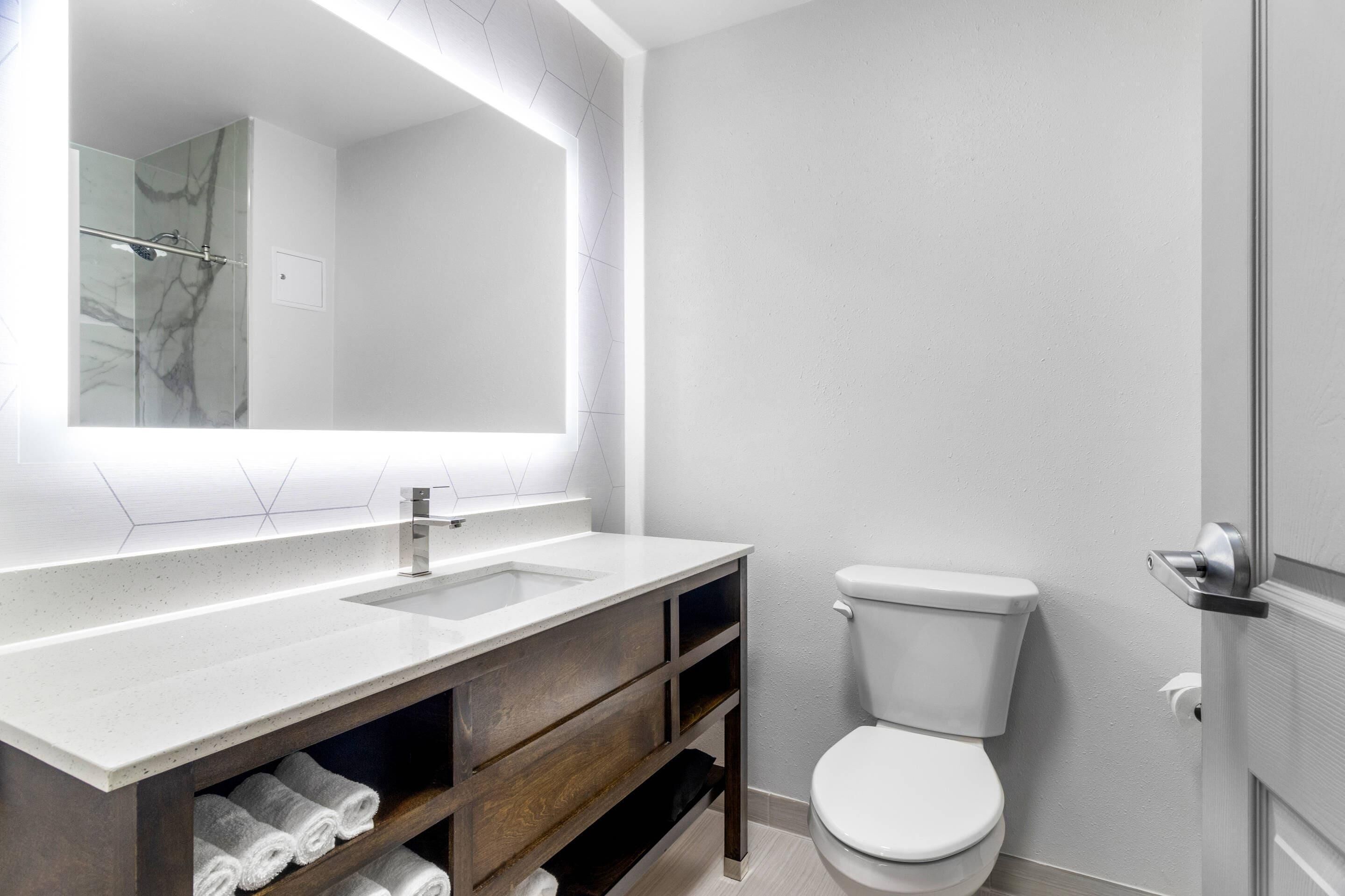 A modern bathroom with a white sink, a large mirror, a toilet, and wooden shelves.