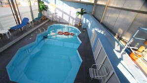 Une piscine intérieure à l’eau bleue, entourée de chaises longues et d’un petit espace aménagé en jardin.