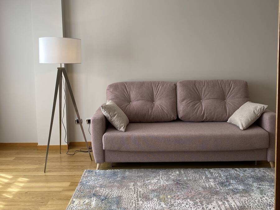 Uma sala de estar moderna com um sofá cinzento, um candeeiro de chão e um tapete estampado.