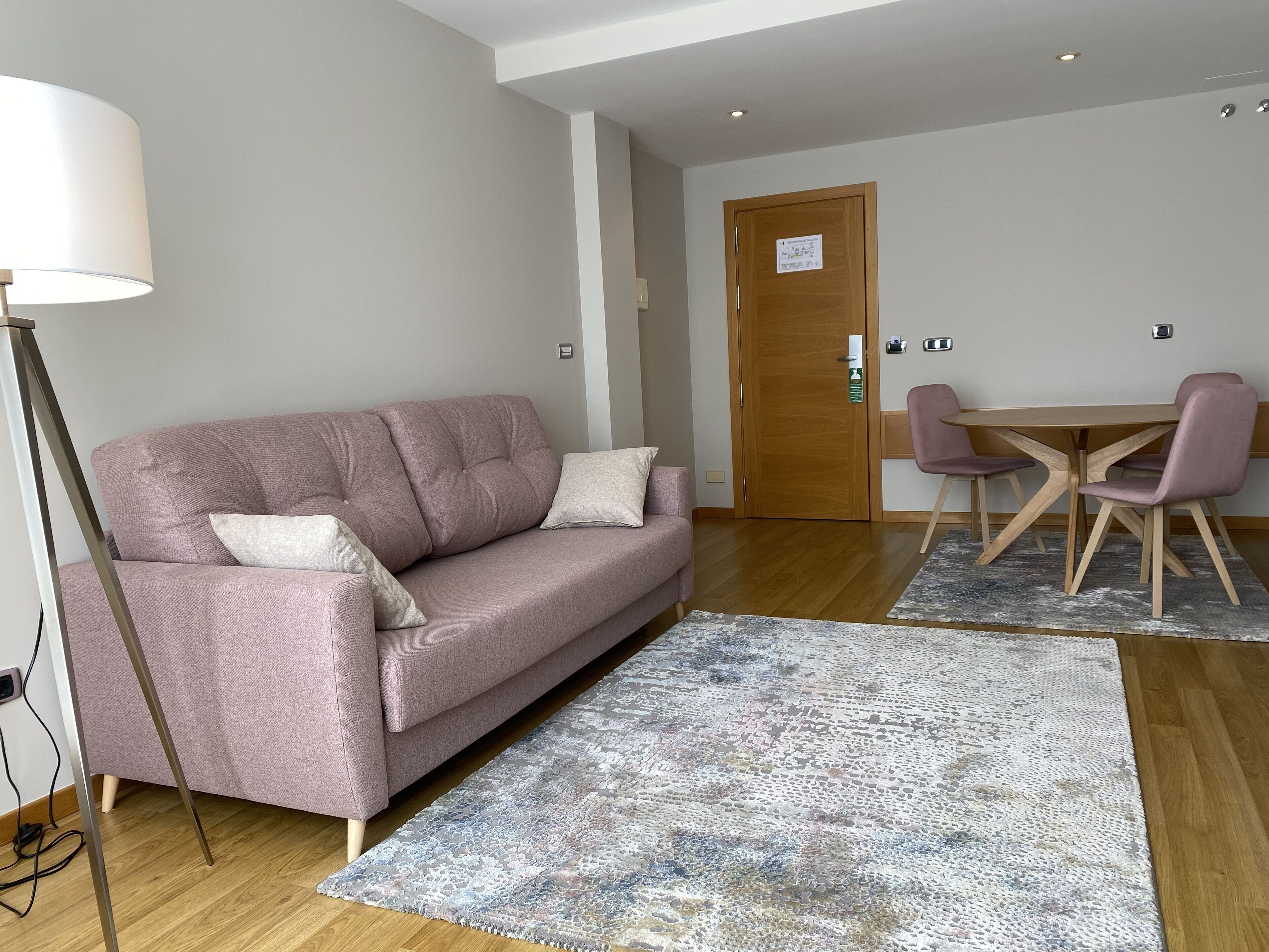 Una sala de estar moderna con un sofá rosa, una mesa de comedor de madera con sillas y una alfombra estampada.