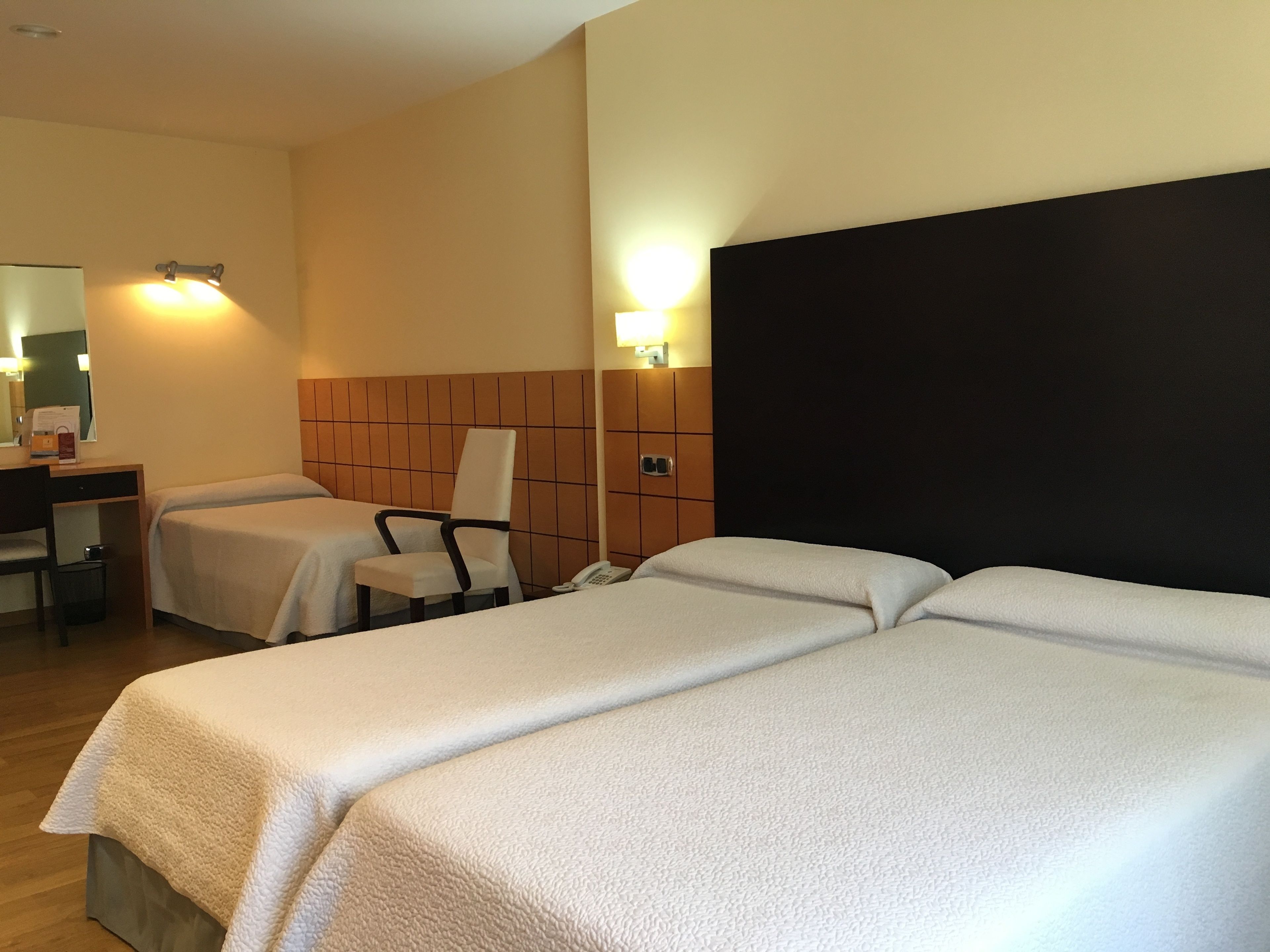 Camera d'albergo con due letti singoli, una scrivania con una sedia, un piccolo tavolino con una lampada e un telefono.