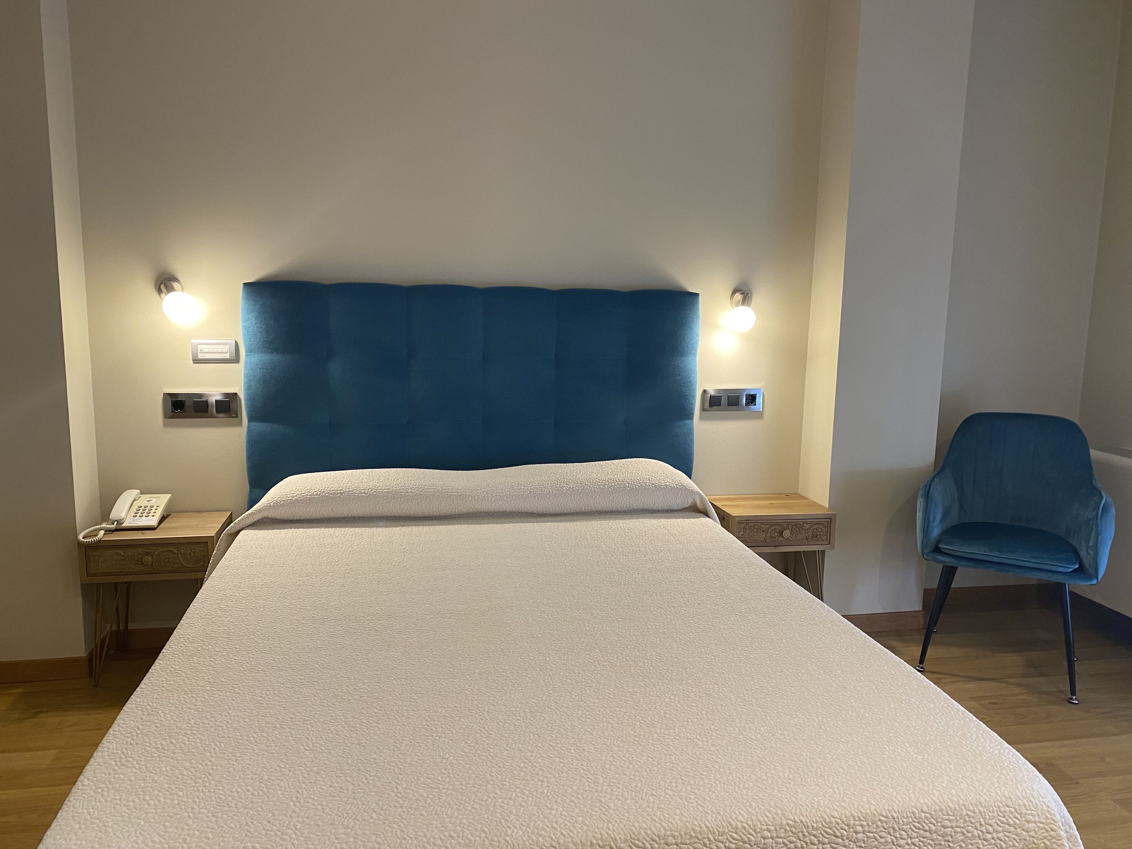 Hotellihuone, jossa on suuri sänky, yöpöytälamput, puhelin, tuoli ja yöpöytä.