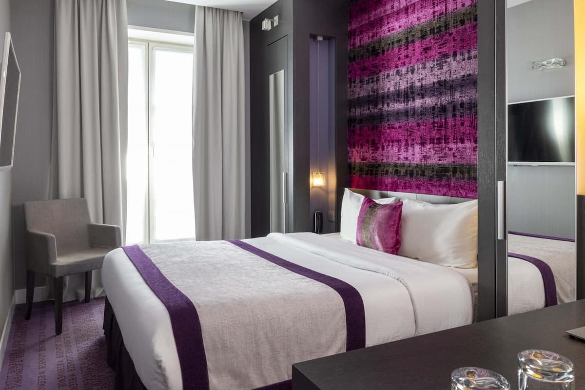 A hotel room with a bed, a chair, a TV, and a wall with a textured pattern.