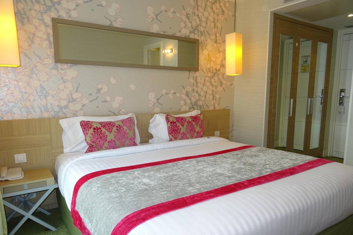 A hotel room with a bed, a nightstand, a mirror, and a wardrobe.