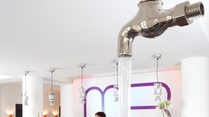 Un mostrador de recepción de diseño moderno, una persona de pie detrás y una original instalación acuática que recuerda a un grifo.