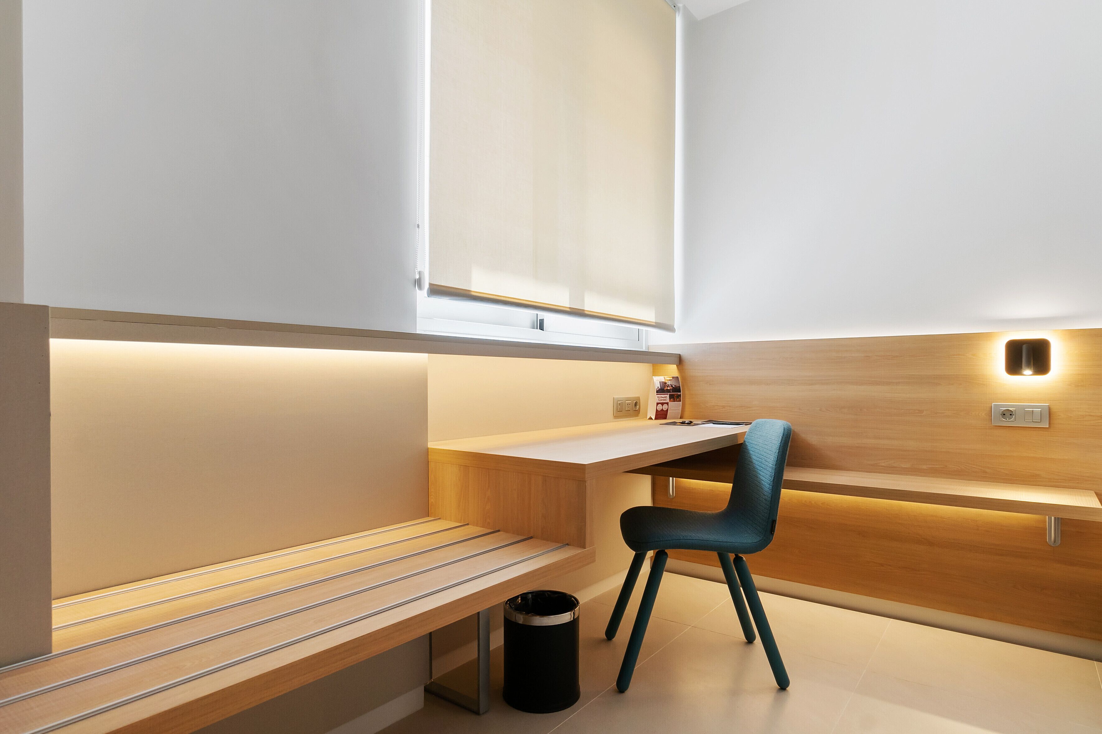 A modern, minimalist room with a wooden desk, a chair, and a bench.