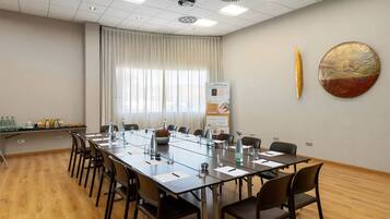 Ein Konferenzraum mit langem Tisch, Stühlen, einem Projektor und einem großen Fenster mit Vorhängen.