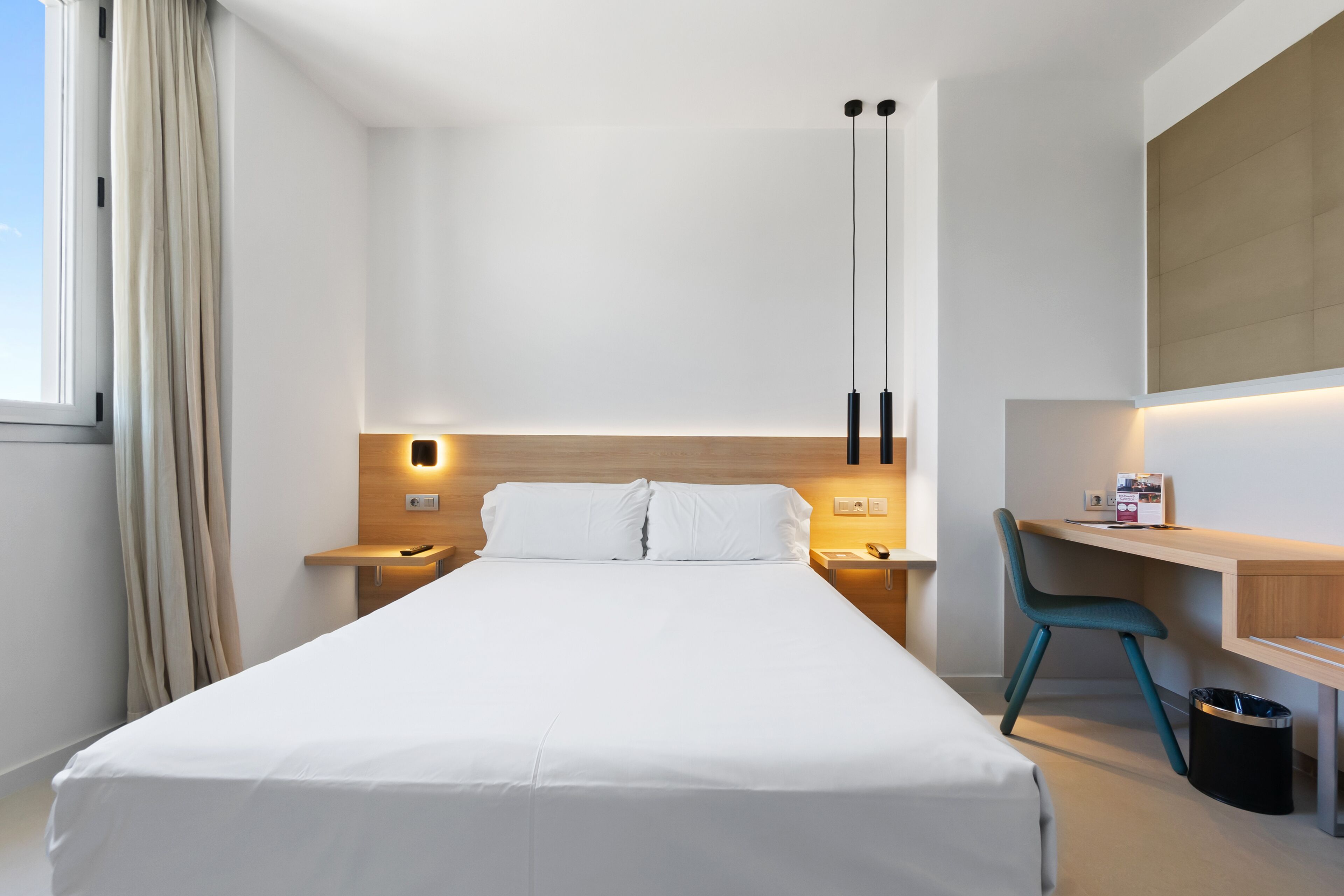 Una habitación de hotel moderna con una cama grande, un escritorio, una silla y un bote de basura.