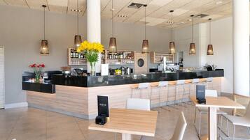 Een moderne bar met een lange toonbank, diverse zitplaatsen en hanglampen.