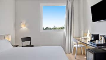 Habitació d'hotel amb un llit, escriptori, cadira, televisió i finestra amb cortines.