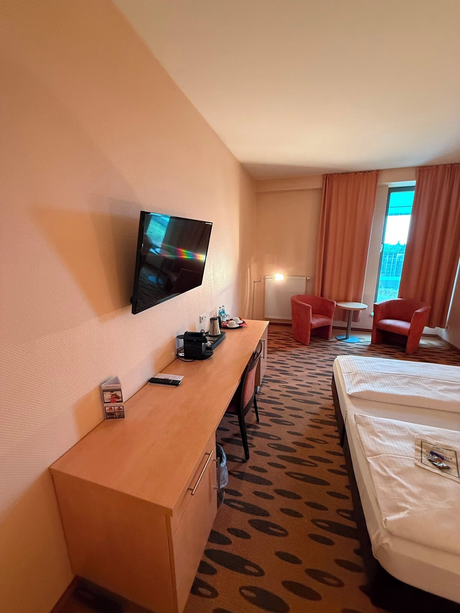 A hotel room with a bed, a desk with a television, a chair, and a small table.