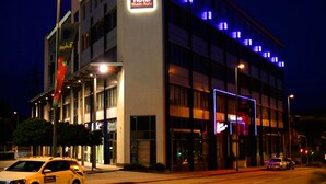 A modern hotel building with a prominent sign, large windows, and a well-lit facade. - Hotel Rhein-Ruhr Bottrop Hauptbahnhof by Mayburgh (Bottrop)