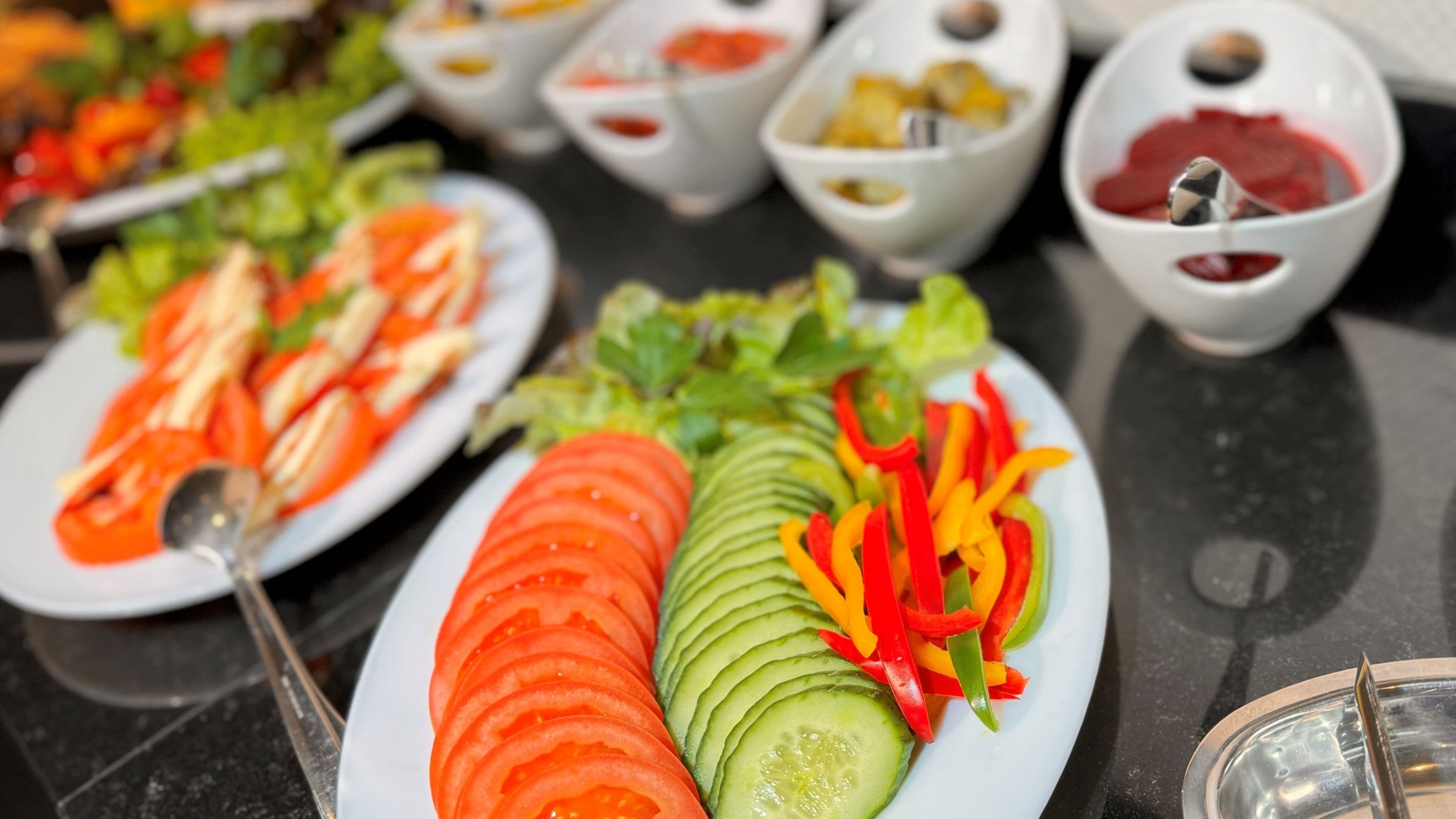 A buffet with various dishes including sliced tomatoes, cucumbers, and bell peppers.