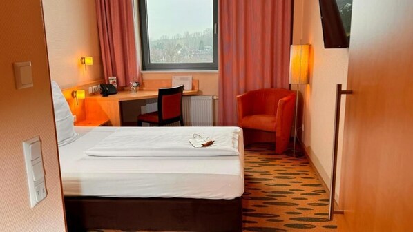 Habitación de hotel con cama, escritorio, silla, ventana y lámpara.