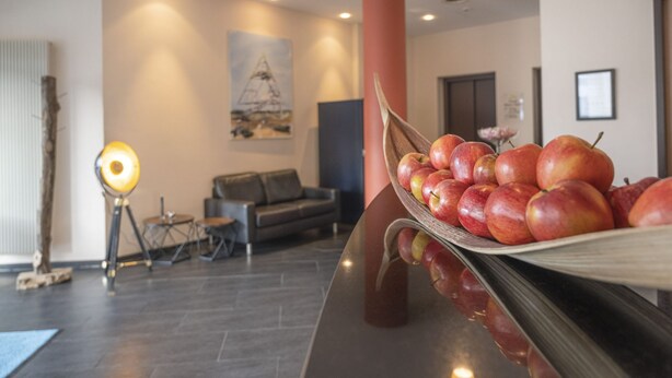 A modern interior with a reception desk, a sofa, and a lamp. - Hotel Rhein-Ruhr Bottrop Hauptbahnhof by Mayburgh (Bottrop)