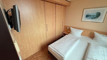 Habitación de hotel con cama, televisor montado en la pared, mesita de noche y un cuadro.