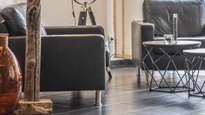 A modern living room with a black sofa, a wooden sculpture, a floor lamp, and a framed artwork on the wall. - Hotel Rhein-Ruhr Bottrop Hauptbahnhof by Mayburgh (Bottrop)