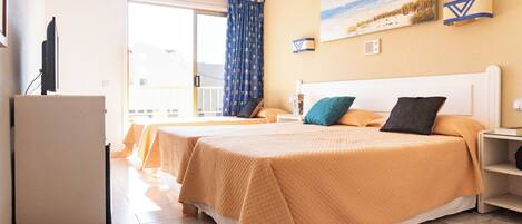 A hotel room with two beds, a TV, a balcony, and a painting of a beach scene.