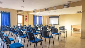 Une salle de conférence avec des rangées de chaises, un écran de projection et un extincteur.