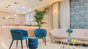 A hotel reception area with a marble reception desk, teal chairs, a beige sofa, and a decorative table with a vase. - Hotel Aeropuerto Sur (Granadilla de Abona)