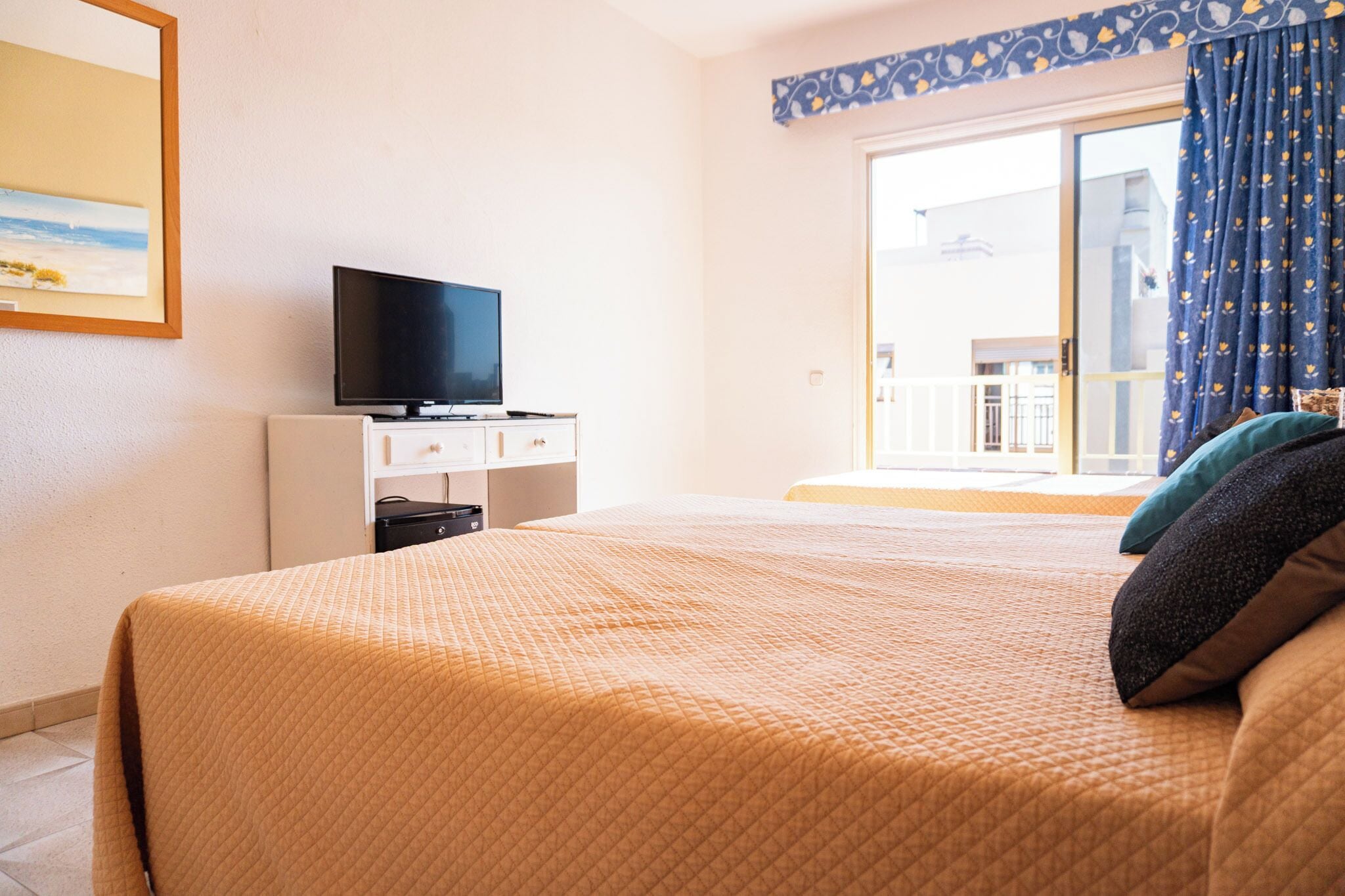 Een hotelkamer met een bed, een televisie op een witte kast, en uitzicht op een gebouw door een glazen deur.