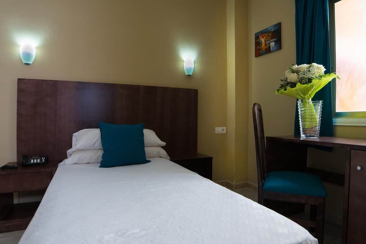 Ein Hotelzimmer mit einem großen Bett, zwei Nachttischen, einem Schreibtisch mit Stuhl, einer Blumenvase und einem Bild an der Wand.