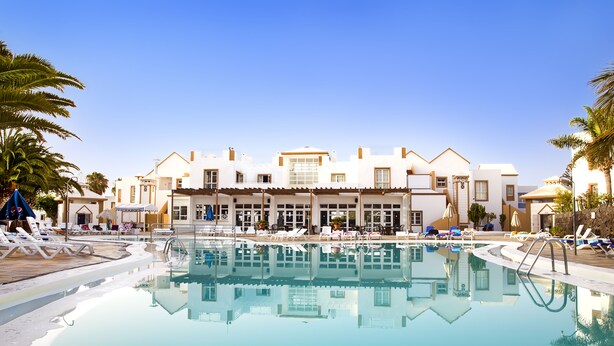 A resort with a large pool, sun loungers, and a building with multiple balconies.